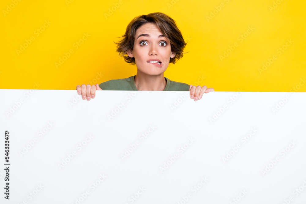 Photo of adorable pretty impressed woman bob hairdo khaki t-shirt hold poster biting lips staring isolated on yellow color background Photo of adorable pretty impressed woman bob hairdo khaki t-shirt hold poster biting lips staring isolated on yellow color background