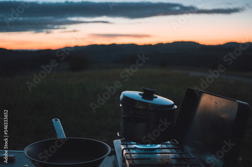 outdoor cooking in beautiful nature after sunset.  blue flame of camping gas stove with pan and pat in nature. Sunset in the background..