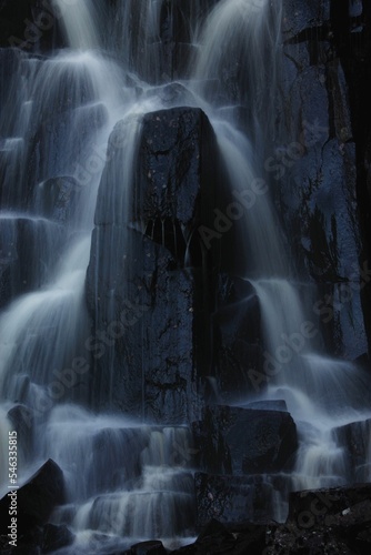 Vertical shot of a waterfall over black rocks