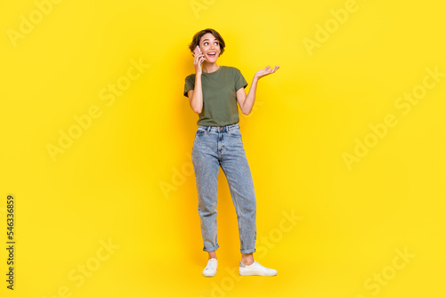Full length photo of adorable positive lady speaking modern telephone interested look empty space isolated on yellow color background © deagreez