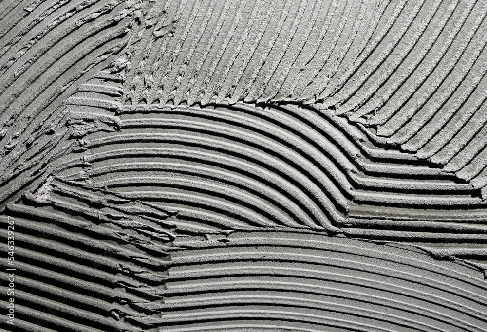 Gray wall glue plaster comb surface prepared for tiling. Tile adhesive  notched trowel patterns. Texture background of tile mortar paste. Grey  cement wall with a linear pattern. Macro shot. Stock Photo