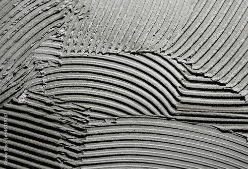 Gray wall glue plaster comb surface prepared for tiling. Tile adhesive notched trowel patterns. Texture background of tile mortar paste. Grey cement wall with a linear pattern. Macro shot. photo