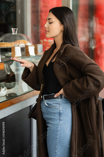 Photography side view of trendy brunette woman touching showcase of patisserie shop in prague