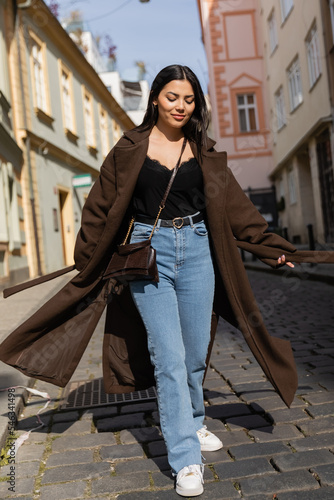 Smiling woman in coat walking on road on urban street in Prague.