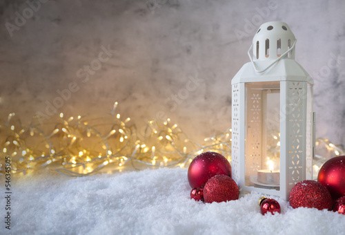 Christmas lantern on the snow next to red textured balls against the background of a lights photo