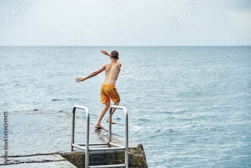 Moments of schoolboy jumping from stone pier with ladder into sea doing tricks in combined image sequence