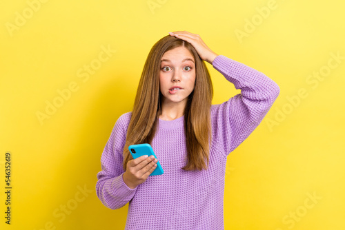 Photo of young scared puzzled girl touch head nervous unexpected reaction oops hold smartphone scam bite lips lose money isolated on yellow color background