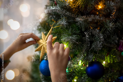 The hands of a child decorating an artificial Christmas tree with a gold star. The atmosphere of preparation for the holiday. The dark key. Zero waste