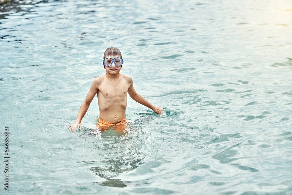 Teenager wearing swimming goggles enjoys summer holidays on sea beach. Excited teen blond boy prepares to swim underwater in goggles