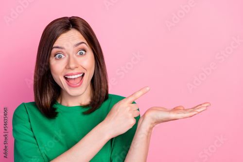 Photo of young attractive woman wear green t-shirt hold hand shock pointing finger empty space isolated on pink color background