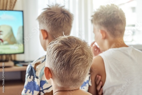 Brothers sitting in hotel room together watch cartoons on TV. Siblings enjoy spending summer holidays relaxing in hotel room and watching movies