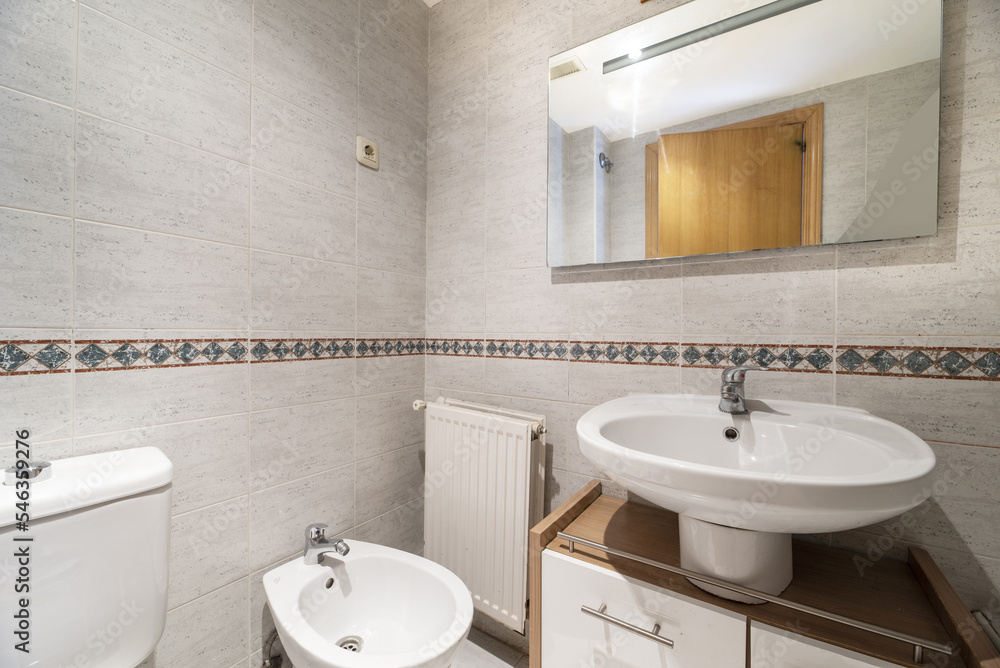 Bathroom with wooden cabinet under the white porcelain sink and frameless mirror on the wall with border Bathroom with wooden cabinet under the white porcelain sink and frameless mirror on the wall with border