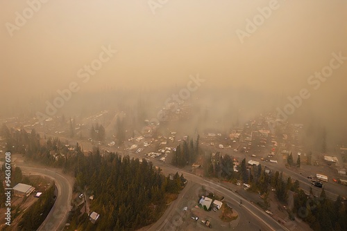 High angle aerial drone shot of small city in Canada slowly fading from sight due to heavy smoke from nearby forest fires in lower interior BC Canada. Traffic and pedestrians seen below.