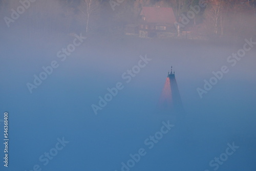 Kirchturmspitze ragt aus dem Nebel