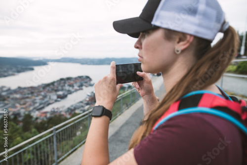 Young tourist woman with cap making a selfie of the view from Floyen mountain over the city of Bergen, Norway. Hiking of Bergen in Norway. 