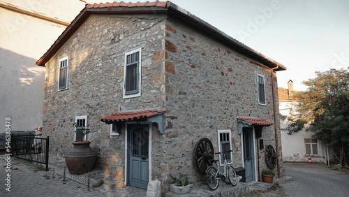 Gökçeada Çanakkale Turkey. July 24, 2022 A historical stone house in Gökçeada town center and a bicycle in front of it, an old cartwheel and a historical amphora next to the building. 