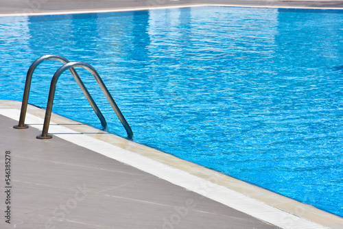 Close up shot of a blue color swimming pool with metal ladder. Modern swimming pool