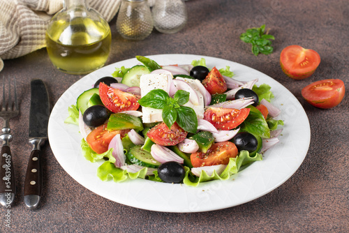 Classic Greek salad from tomatoes  cucumbers  sweet pepper  olives  basil and feta cheese on white plate