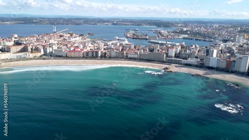 Drone point of view of Galician city A Coruna. View of famous beach Orzan. In background the city center and the harbour area. Drone forward and tilt up. Travel destination in Northwest of Spain 