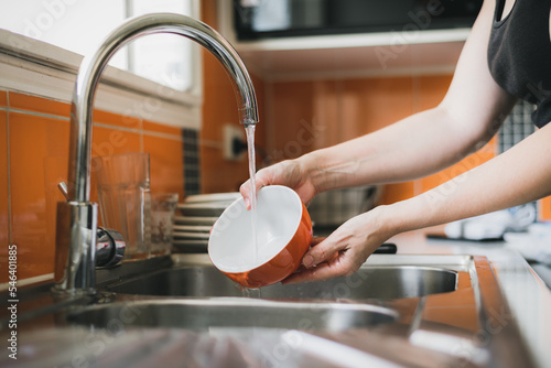 Woman washing dishes in kitchen sink, close up of hands rinsing bowl