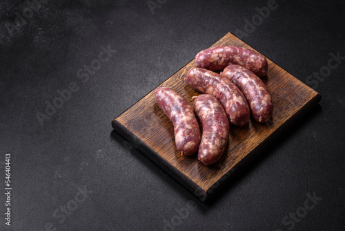 Raw pork sausages grill with spices and herbs on a dark concrete table