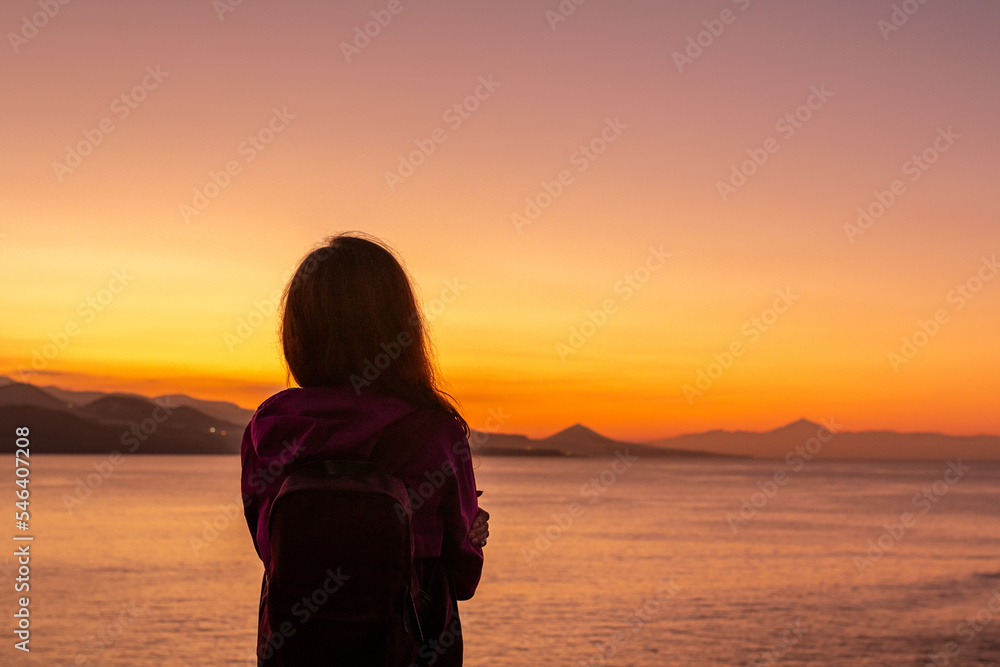 Silhouette of a young woman against colorful sunset landscape. View over Atlantic Ocean on Teide volcano in Tenerife as seen from Las Palmas de Gran Canaria (Spain). New goals and plans for new year.