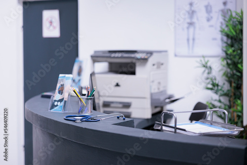 Medical exams on empty front desk of unoccupied medical office. Patient reception area with counter, files and office, technological articles. Stethoscope on table with informational brochures.