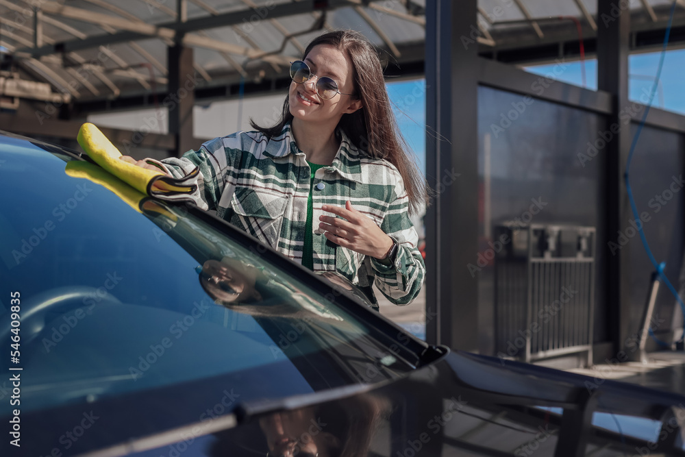 A young female cleaning and polishing her car with yellow microfiber cloth. Concept of car taking care