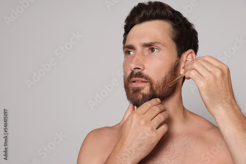 Man applying oil onto beard on grey background. Space for text
