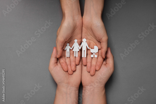 Couple holding paper family figures on grey background, top view. Insurance concept