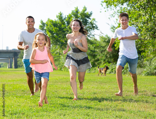 Happy family of four running on grass at summer park. High quality photo