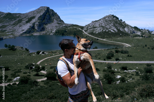 latin guy in sunglasses with a big dog in his arms near the lake and mountains, covadonga asturias, spain