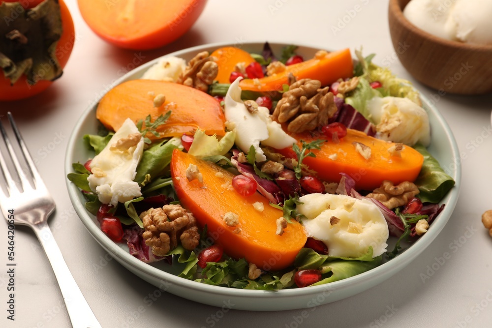Delicious persimmon salad with cheese and pomegranate served on white table Delicious persimmon salad with cheese and pomegranate served on white table