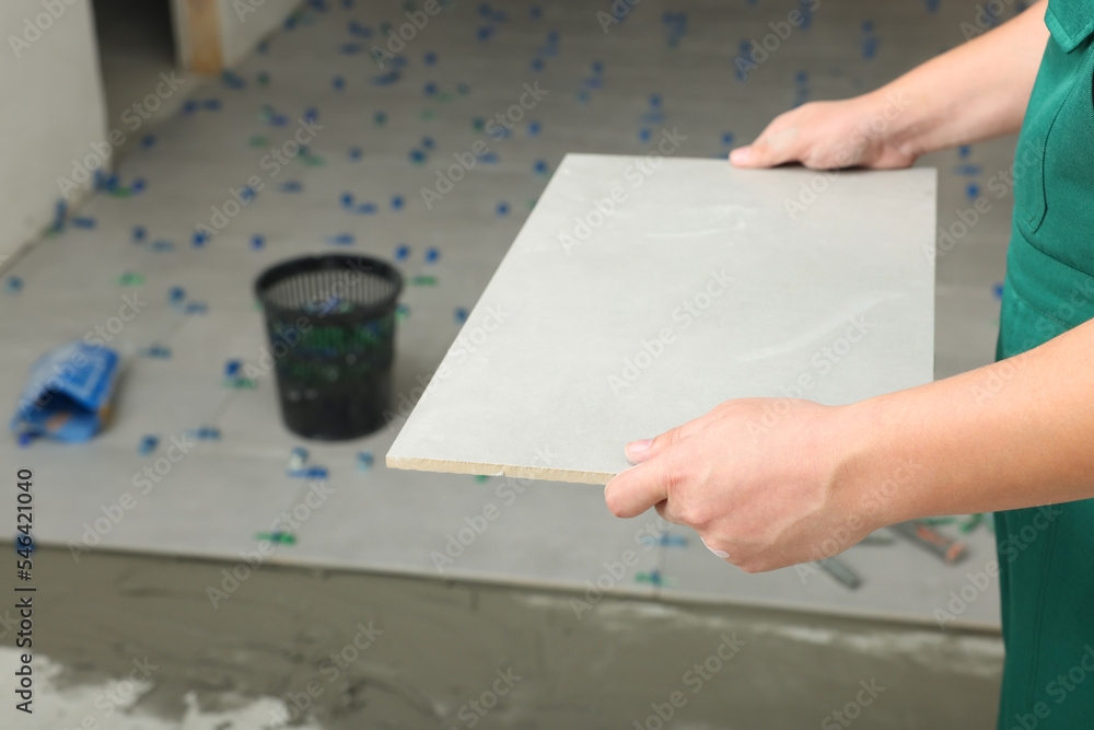 Worker holding tile near adhesive mix on floor, closeup Worker holding tile near adhesive mix on floor, closeup