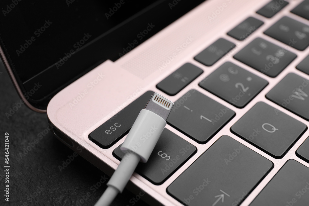 USB cable with lightning connector and laptop on black slate table, closeup USB cable with lightning connector and laptop on black slate table, closeup