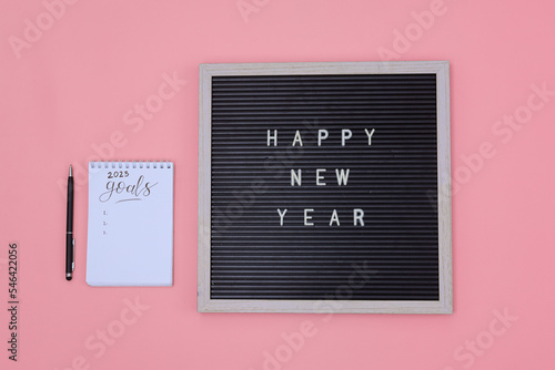Letter board with Happy New Year message and 2023 goals on notebook isolated in pink background.