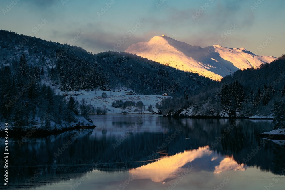 Obraz premium Beautiful view of a lake surrounded by tree-covered snowy mountains under a clear blue sky