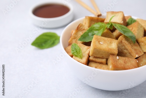 Delicious fried tofu, basil and sesame seeds served on light grey table, closeup. Space for text