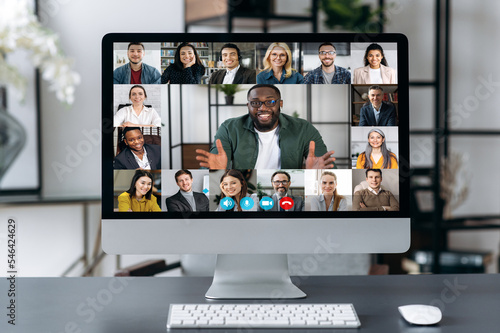 Virtual business meeting, online briefing, brainstorm. A computer monitor is on the desktop, on the screen is many different multiracial business partners gathered in a video conference