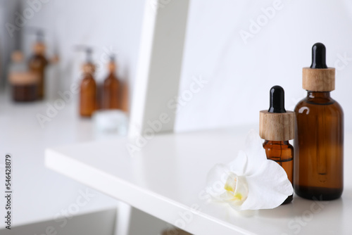 Bottles of essential oil and orchid flower on white shelf in bathroom. Space for text