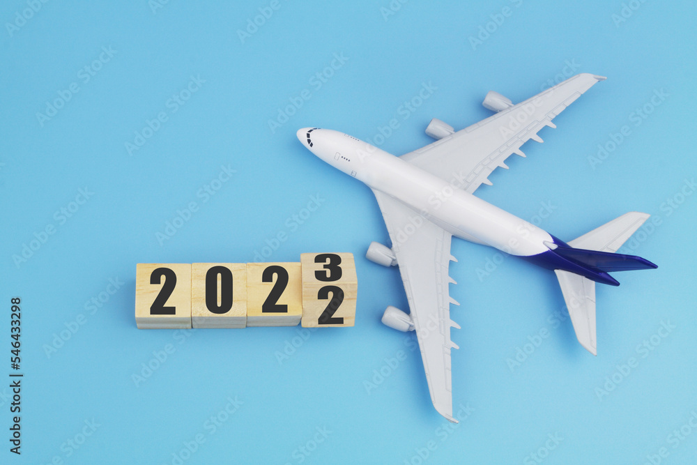 Airplane model and cubes with 2022 and 2023 on blue background. Travel in new year 2023. Airplane model and cubes with 2022 and 2023 on blue background. Travel in new year 2023.
