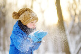 Little boy blowing snow from his hands. Child enjoy walking in the park on snowy day. Baby having fun during snowfall. Outdoor winter activities for kids.
