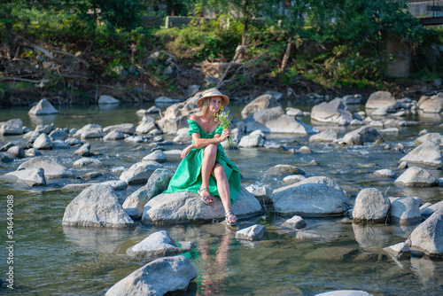 a girl in a hat is sitting on the rocks by the river