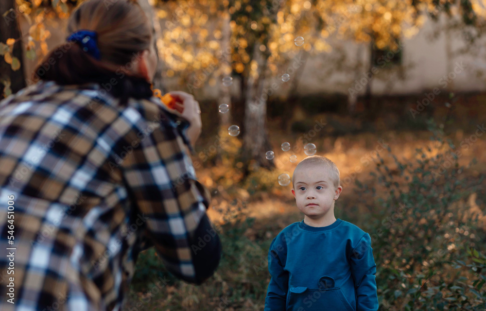 Little boy with Down syndrome walks in the park with his mother, soap bubbles Little boy with Down syndrome walks in the park with his mother, soap bubbles