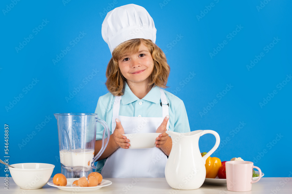 Portrait of a 7, 8 years old child in cook cap and apron making fruit salad and cooking food in kitchen. Cute little blonde happy smiling chef. Portrait of a 7, 8 years old child in cook cap and apron making fruit salad and cooking food in kitchen. Cute little blonde happy smiling chef.