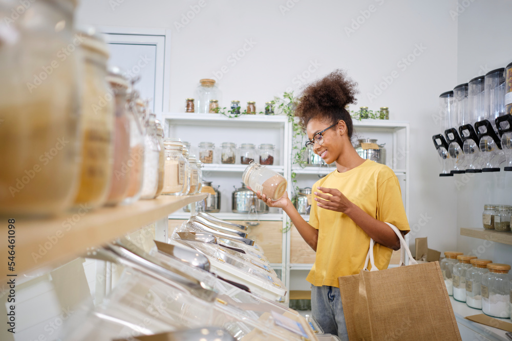 Φωτογραφία Young African American woman is choosing and shopping for organic products in refill store with reusable bag, zero-waste grocery, and plastic-free, eco environment-friendly, sustainable lifestyles