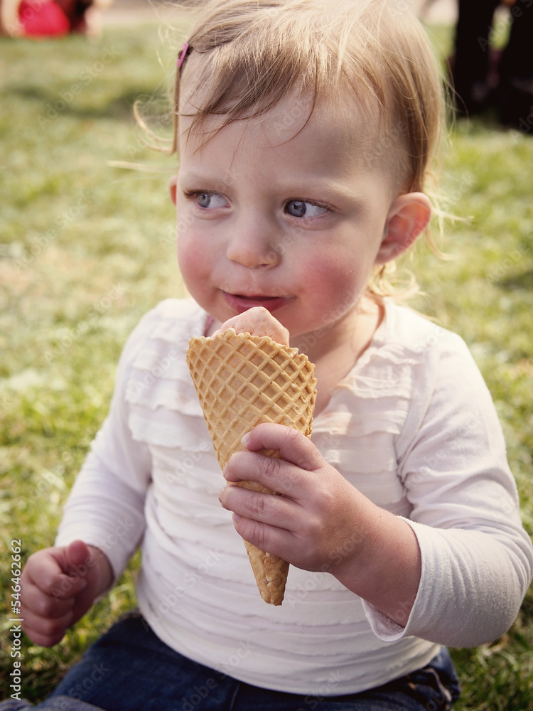 Young blond 2 year old girl eating strawberry ice cream in a waffle cone. Young blond 2 year old girl eating strawberry ice cream in a waffle cone.