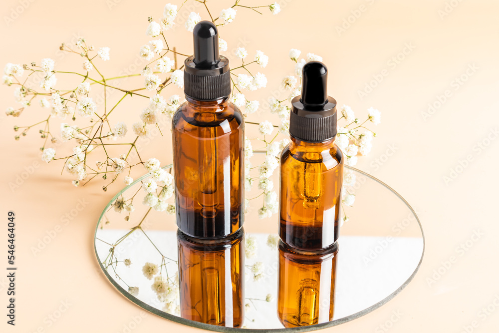 cosmetic bottles made of amber glass with a dropper stand on a round mirror with a white gypsophila. front view. layout of the cosmetic brand. cosmetic bottles made of amber glass with a dropper stand on a round mirror with a white gypsophila. front view. layout of the cosmetic brand.