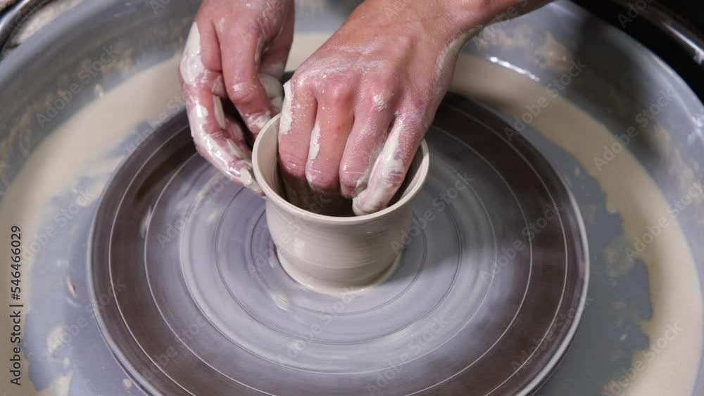 Female potter with soiled hands, forming a goblet from a piece of white clay on a potter's wheel. Close-up. Pottery Workshop. The concept of handwork, art, and craft Female potter with soiled hands, forming a goblet from a piece of white clay on a potter's wheel. Close-up. Pottery Workshop. The concept of handwork, art, and craft