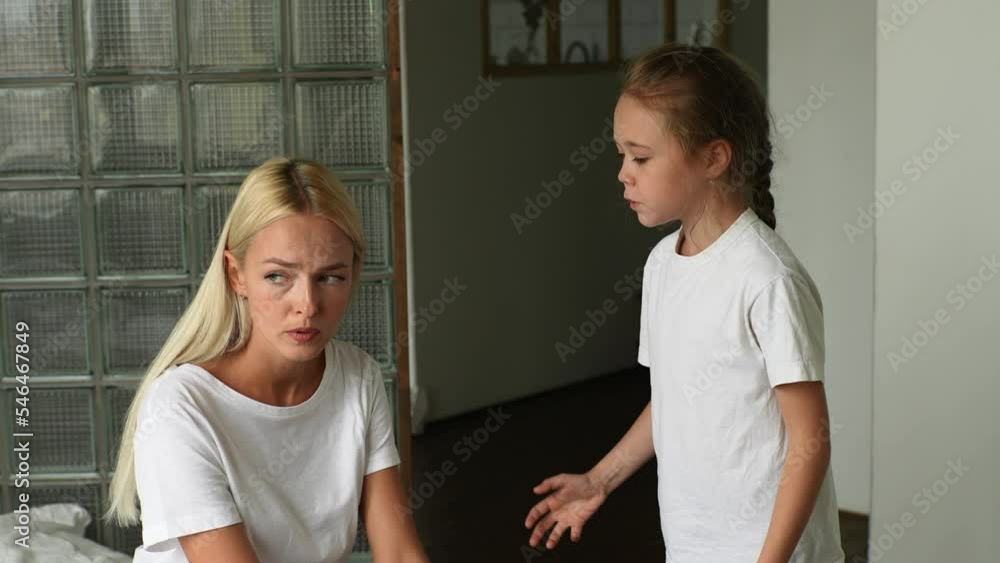 Portrait of standing angry little child daughter scolding, raising voice, scream to sad young mother sitting on sofa at home. Concept of mom-child problem in preteen years. Shooting in slow motion. Portrait of standing angry little child daughter scolding, raising voice, scream to sad young mother sitting on sofa at home. Concept of mom-child problem in preteen years. Shooting in slow motion.